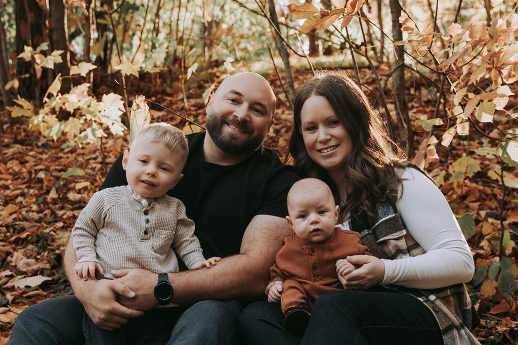 A father and mother pose with their two young sons with fall leaves behind them